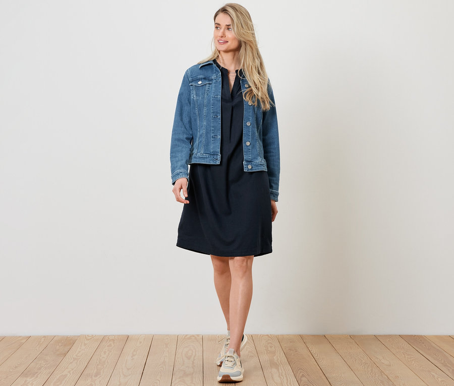 Žena má na sobě džínovou bundu a lněné šaty.