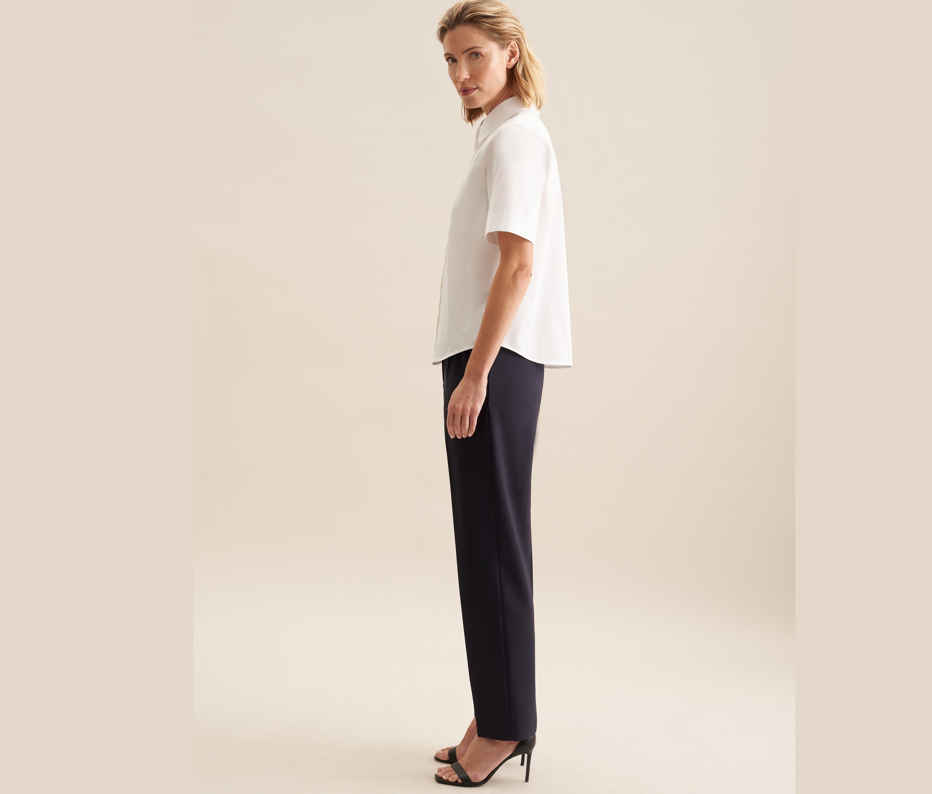 Žena pózuje v bílé halence s krátkým rukávem Seidensticker a tmavě modrých kalhotách.