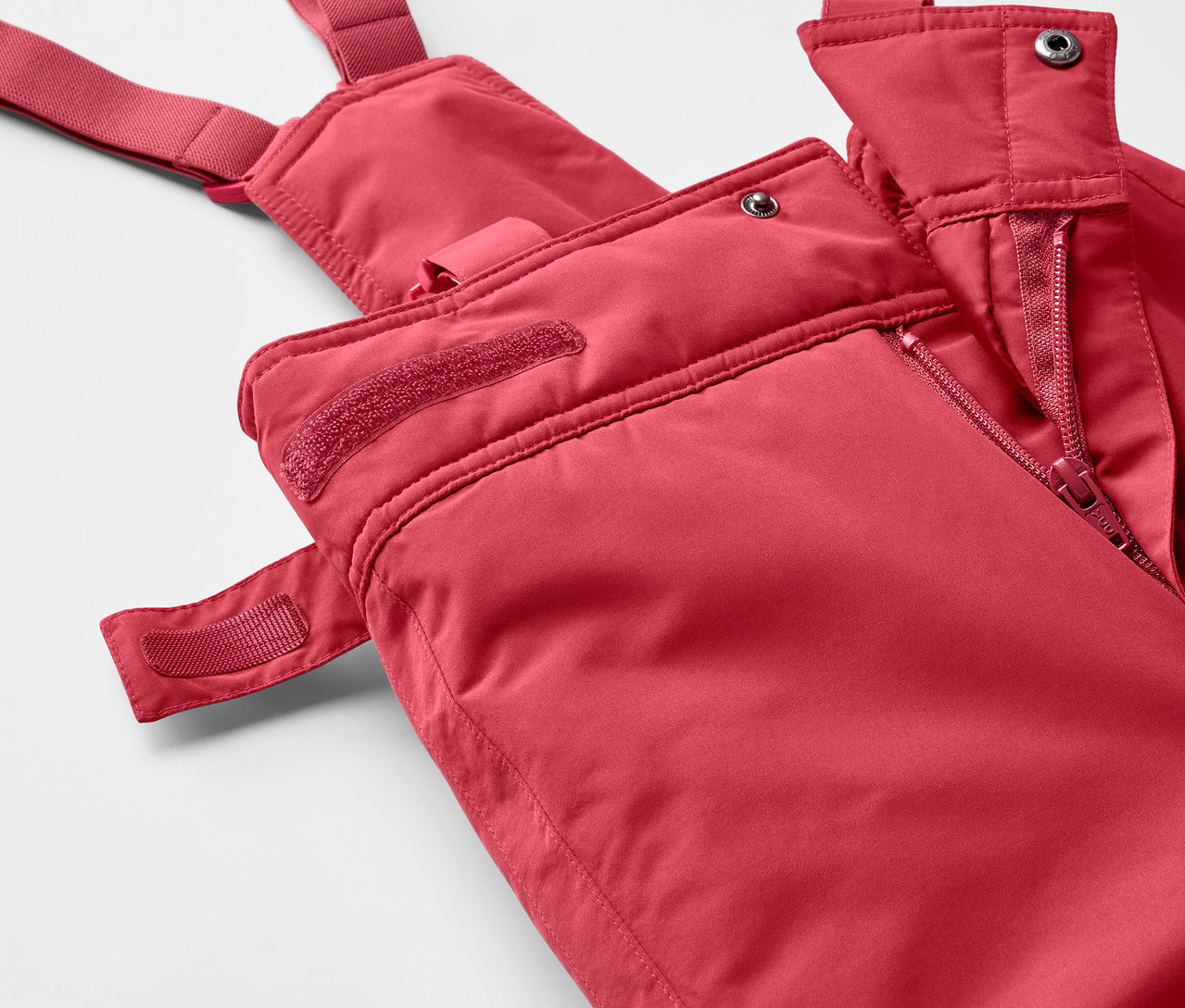 Detail červených lyžařských kalhot s laclem se zipem.