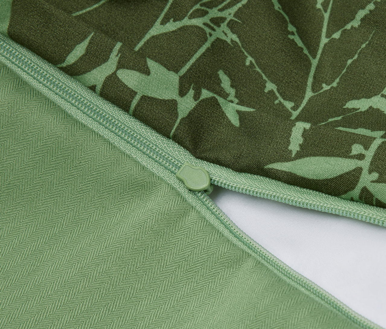 Detail zeleného povlaku na polštář s květinovým vzorem a zipem.