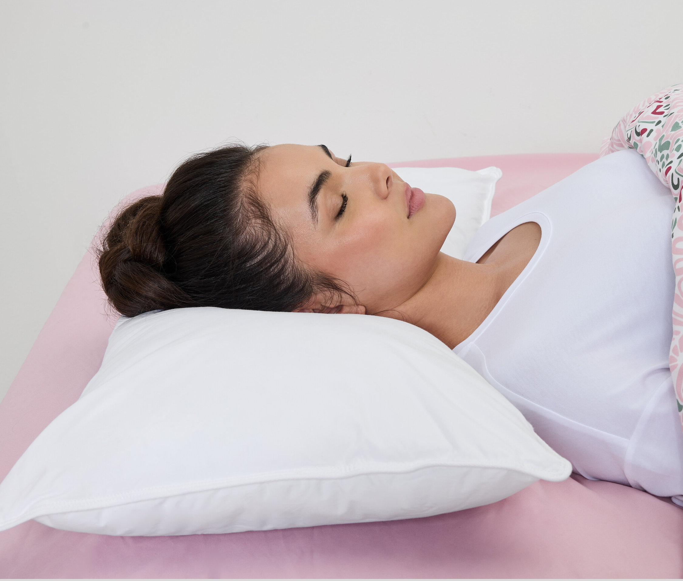 Žena spí na bílém vodním polštáři irisette® na růžovém prostěradle.