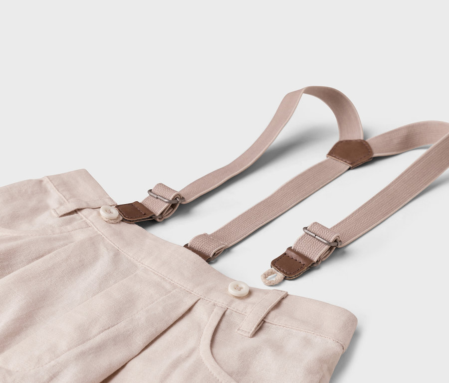 Detail béžových látkových kalhot s šlemi na bílém pozadí.