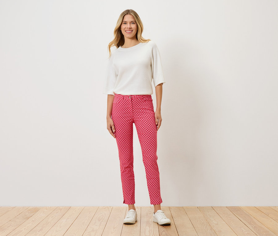 Žena stojí a má na sobě bílý top, červené kalhoty s puntíkovaným vzorem a bílé boty.