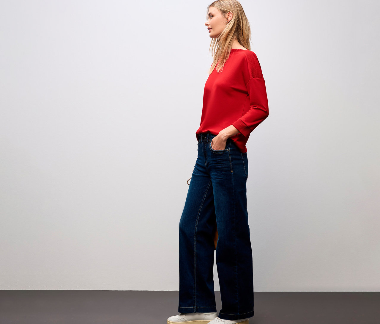 Žena v červeném tričku Street One s žebrovanými detaily a v džínách.