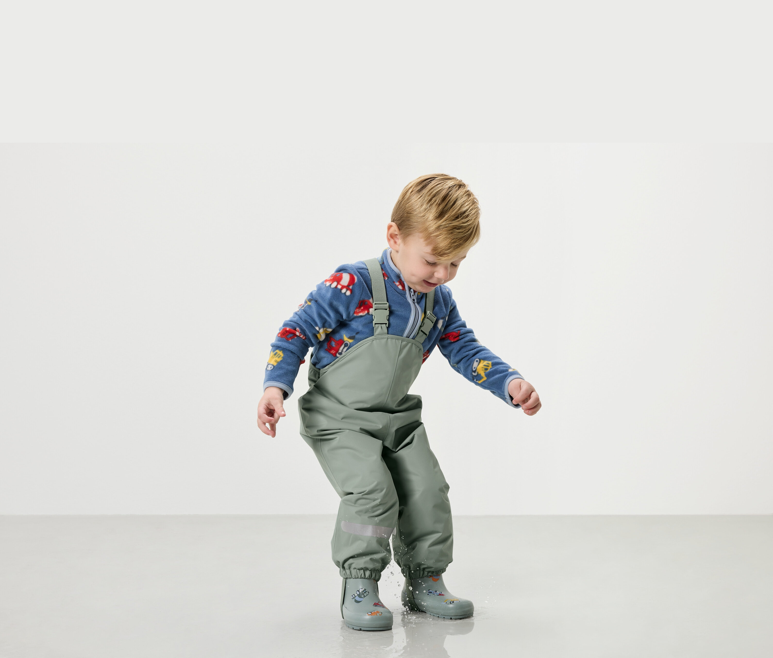 Chlapec si hraje ve vodě v zeleném dešťovém oblečení a holínkách.