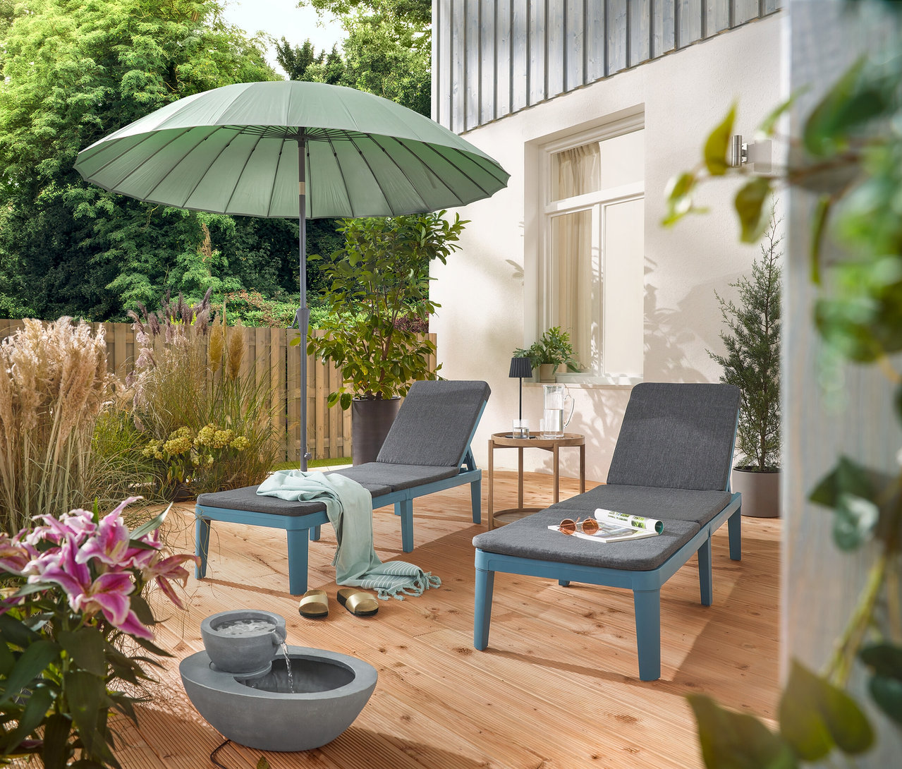 Na terase jsou dvě lehátka pod světle šedým slunečníkem Leco Shanghai a vedle solární zahradní fontány.