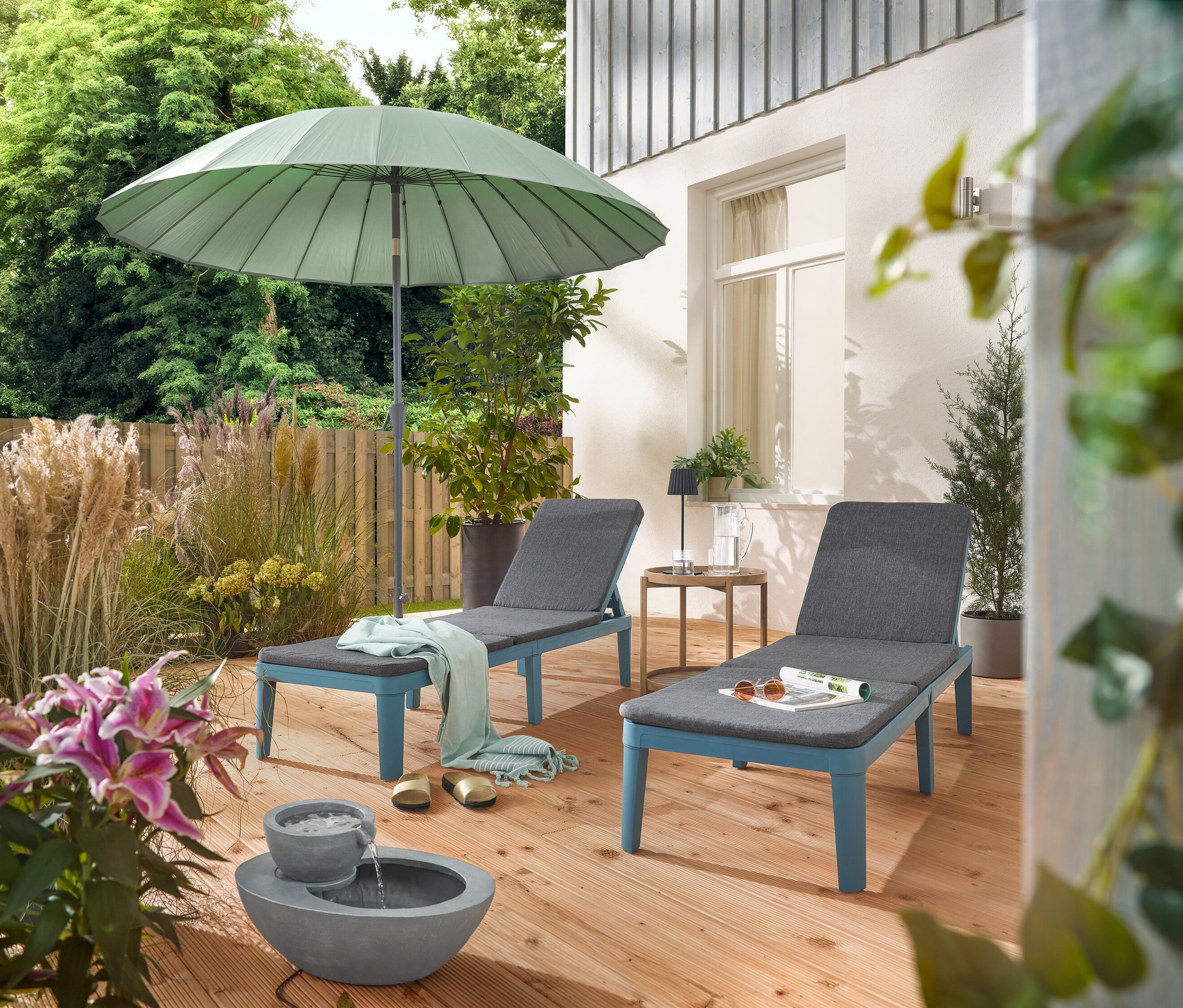 Na terase jsou dvě lehátka pod světle šedým slunečníkem Leco Shanghai a vedle solární zahradní fontány.