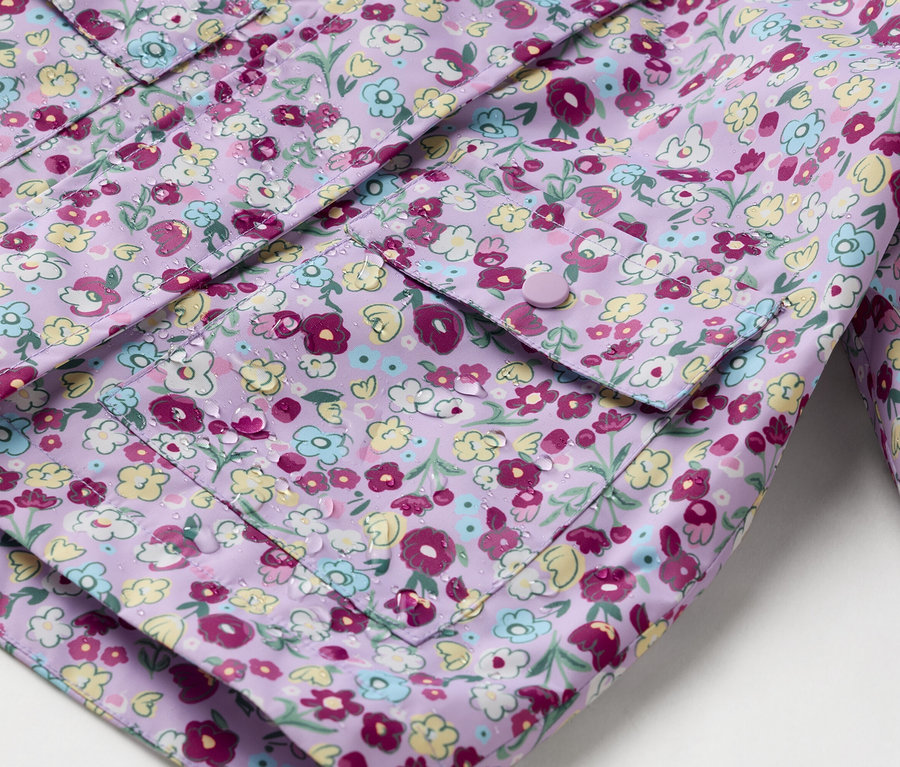Detail fialové pláštěnky s květinovým potiskem a našitými kapsami zapínanými na knoflíky.