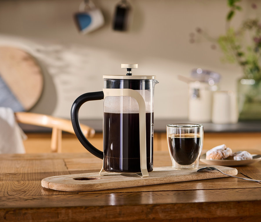 Béžová french press konvička (800 ml, 6 šálků) stojí na dřevěném podnosu vedle šálku kávy.