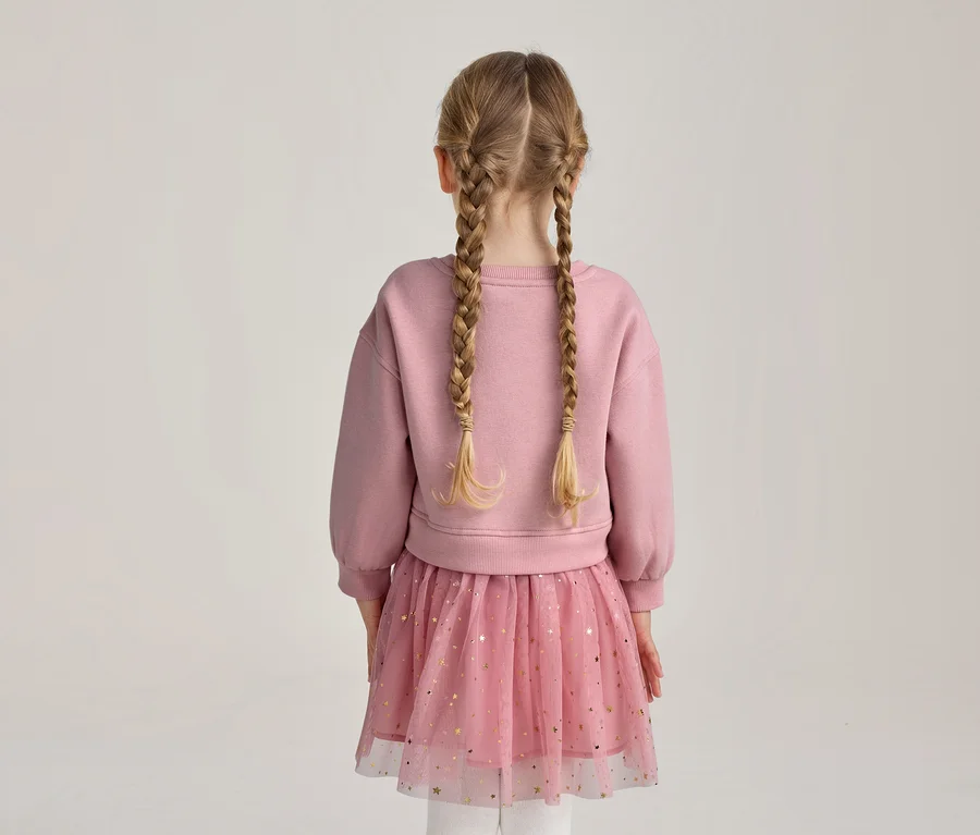 Dívka zezadu s blond copy, v růžové mikině a růžové tylové sukni se zlatými hvězdami.