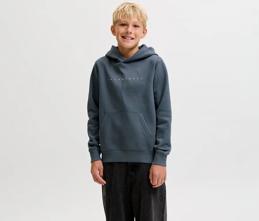 Usmívající se chlapec v tmavě šedé mikině s kapucí Jack & Jones Star s klokaní kapsou a tmavými kalhotami.