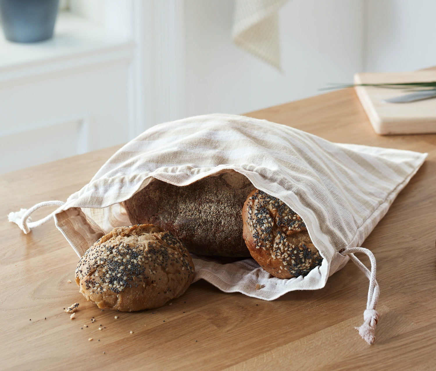 Chléb a dva bochníky v proužkovaném sáčku na chléb na dřevěném stole.
