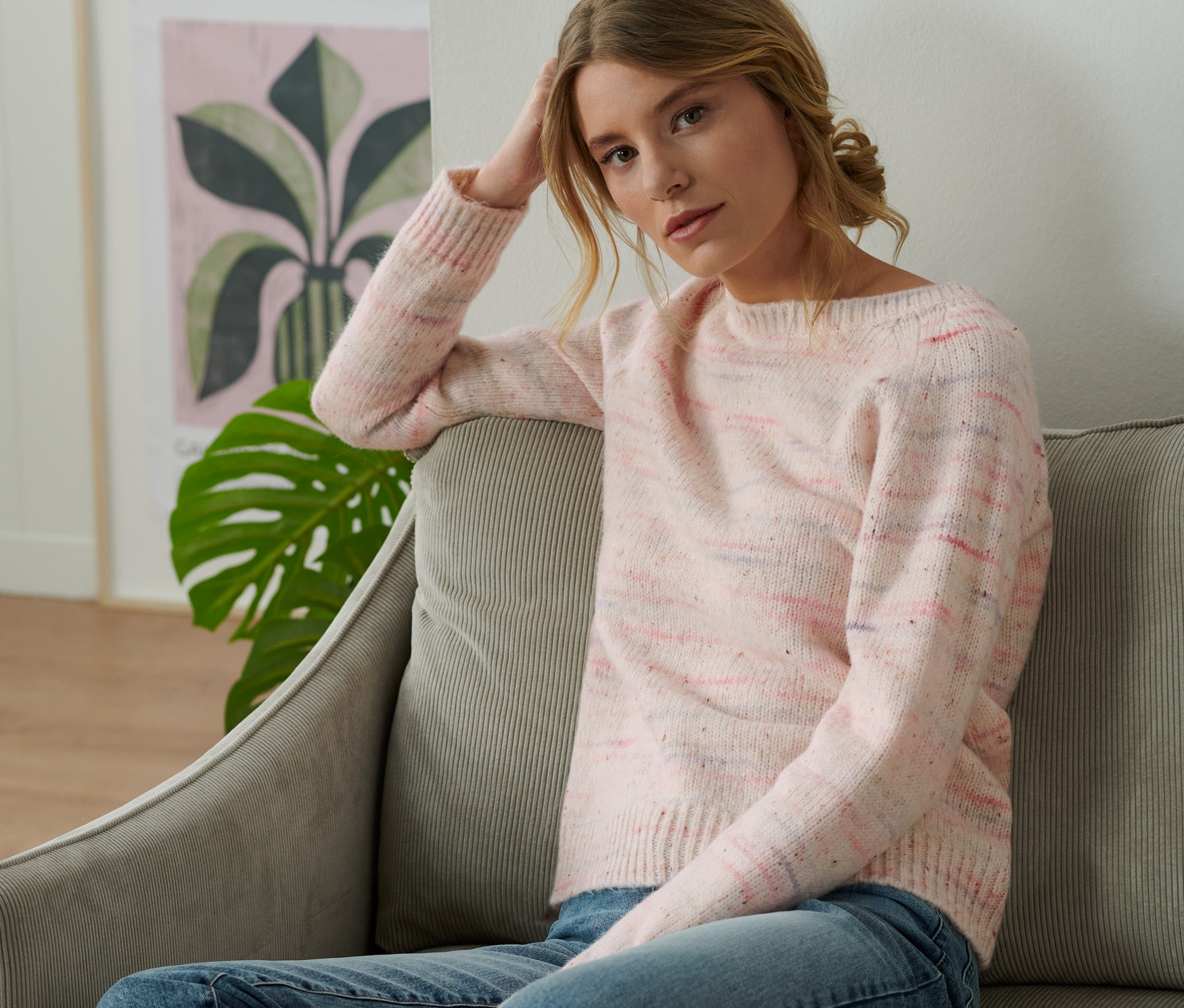 Žena sedí na pohovce a má na sobě svetr z hrubé pleteniny s efektní přízí.