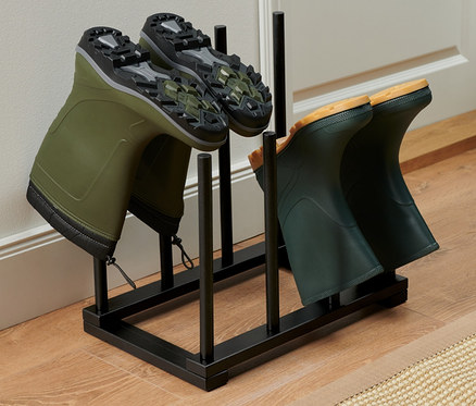 Dva páry zelených holínek jsou umístěny na černém stojanu na boty.