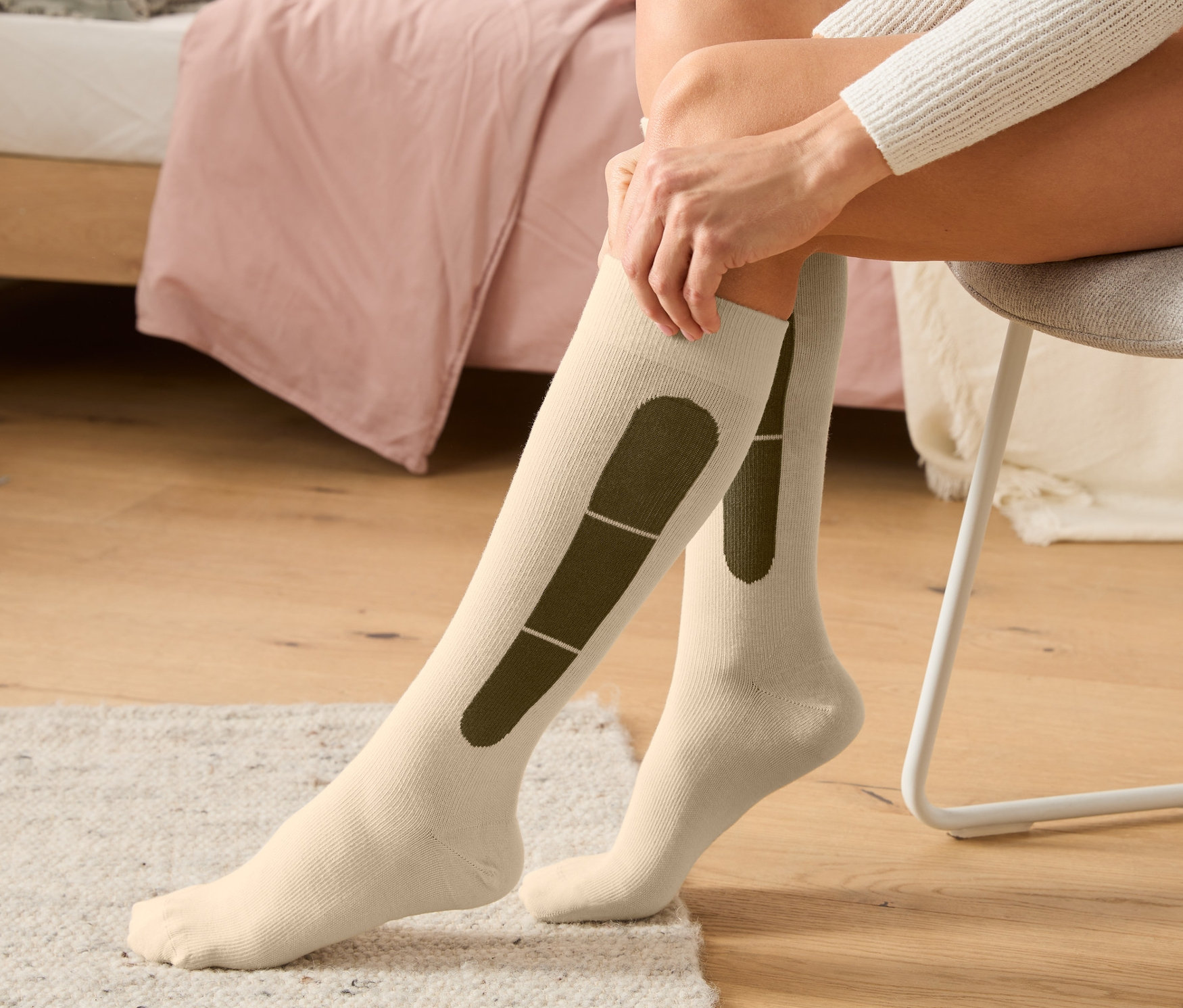 Žena sedí na židli a natahuje si béžové cestovní kompresní punčochy.
