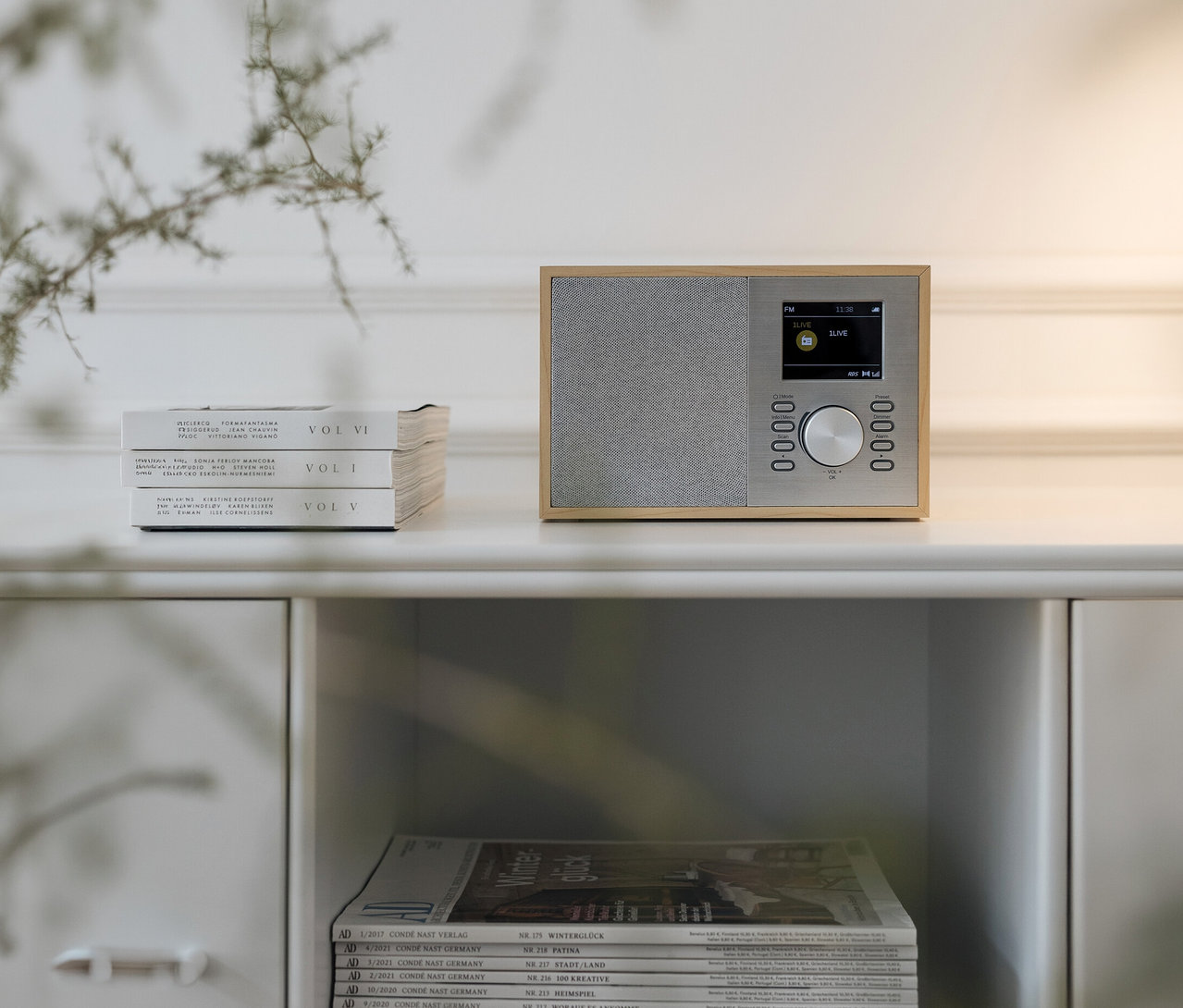 Digitální rádio DAB+/FM s Bluetooth® stojí na bílé skříňce vedle tří knih. Pod nimi leží časopisy.