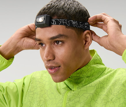 Muž si upravuje na čele čelovku a má na sobě zelenou bundu.