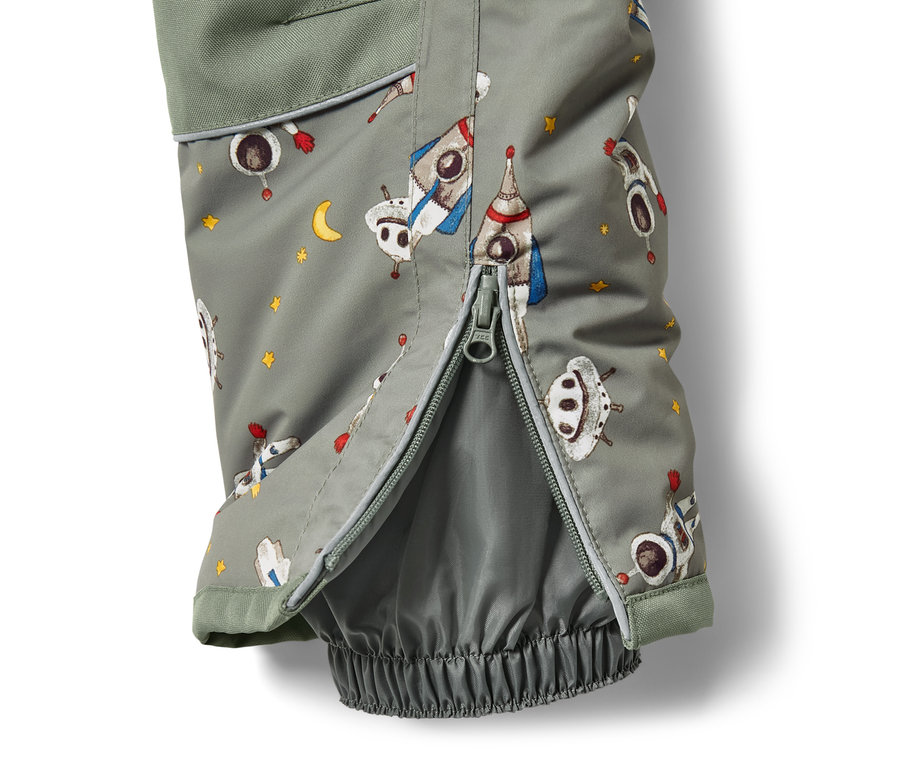 Detail dětské zimní kombinézy s potiskem vesmírných lodí a rozepnutým zipem.