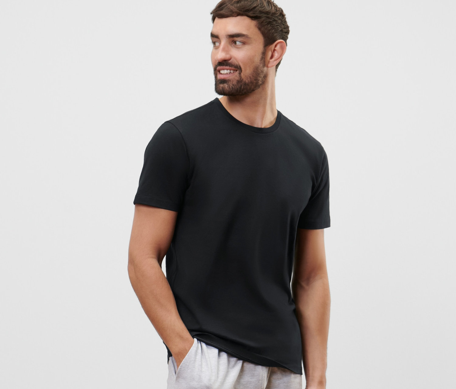 Muž s vousy má na sobě černé tričko s kulatým výstřihem z 2 ks soupravy a šedé šortky.