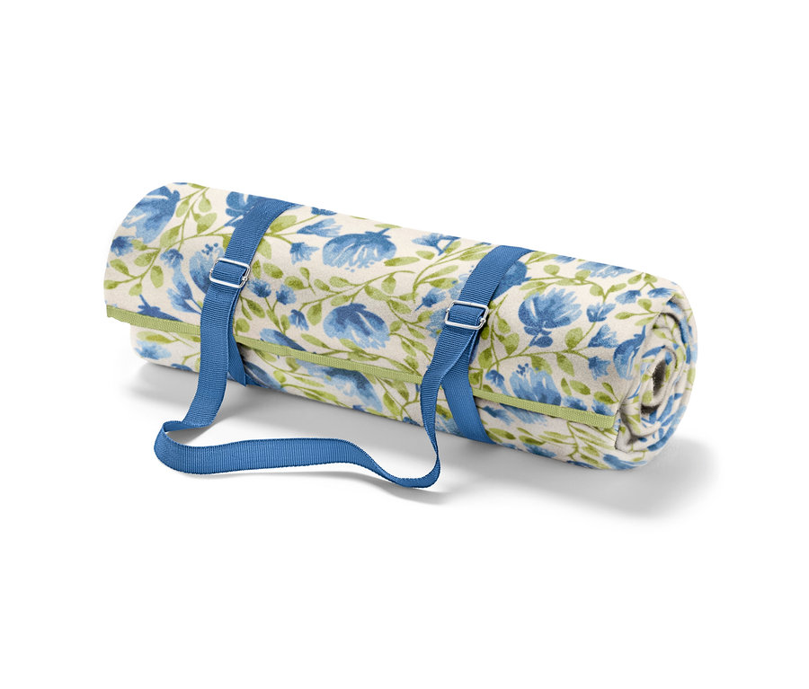 Srolovaná malá pikniková deka s modrými květy a zelenými stonky, upevněná modrými popruhy.