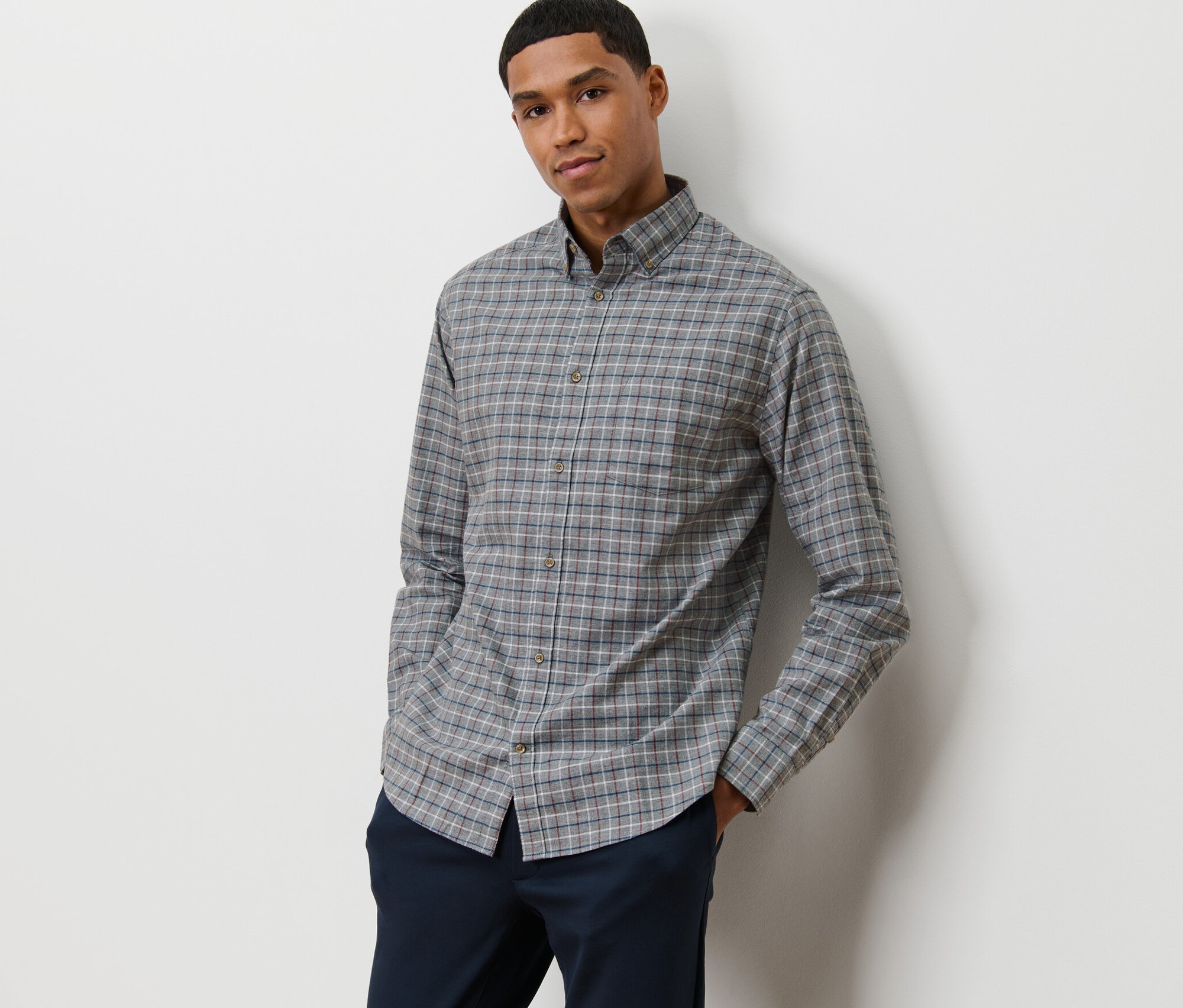Muž pózuje v šedé flanelové košili.