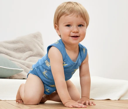 Usmívající se kojenec na kolenou nosí modré body pro miminka s potiskem.