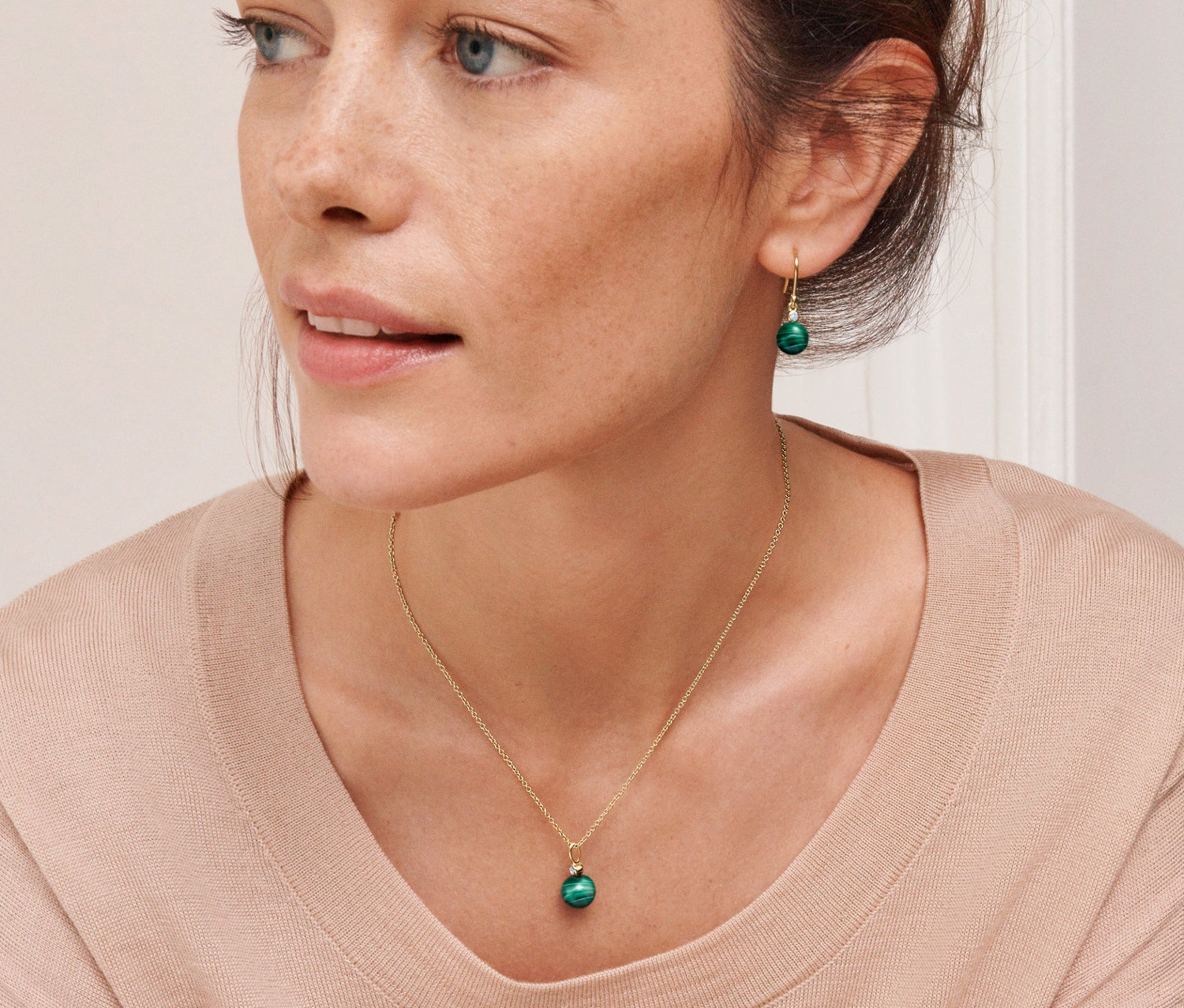 Žena má na sobě zlacený stříbrný řetízek a náušnice s malachitem.