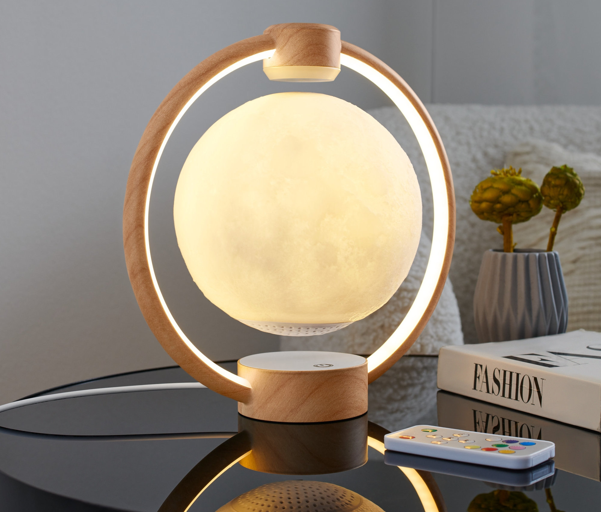Levitující reproduktor »Měsíc« s LED Bluetooth® stojí na nočním stolku vedle knihy a dálkového ovládání.
