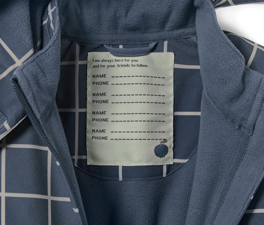 Detail dětské softshellové kombinézy s kostkovaným vzorem a štítkem pro jméno a telefonní číslo.