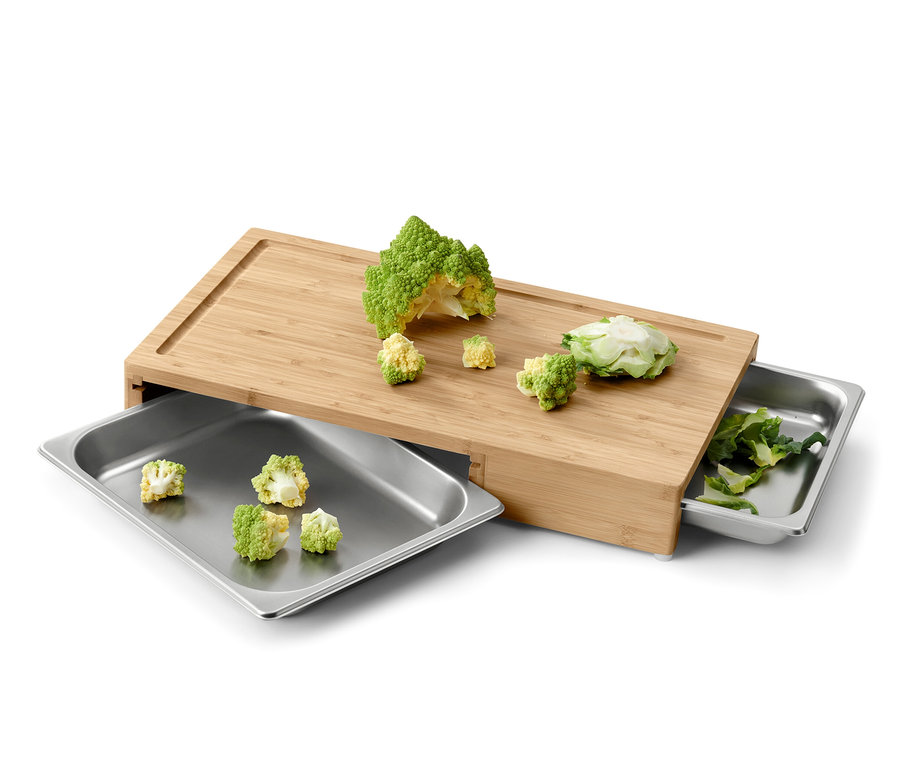 Řezací prkénko s nakrájenou zeleninou a dvěma kovovými tácky.