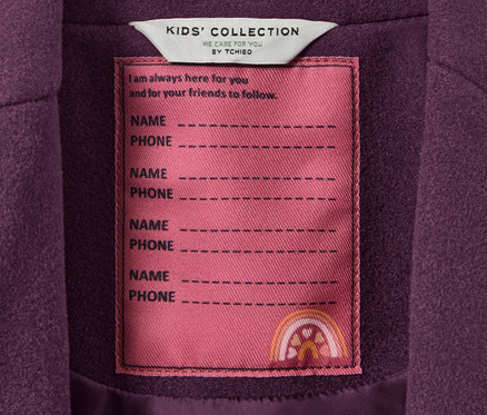 Detail dětského kabátku s cedulkou KIDS' COLLECTION s místem pro jméno a telefon.