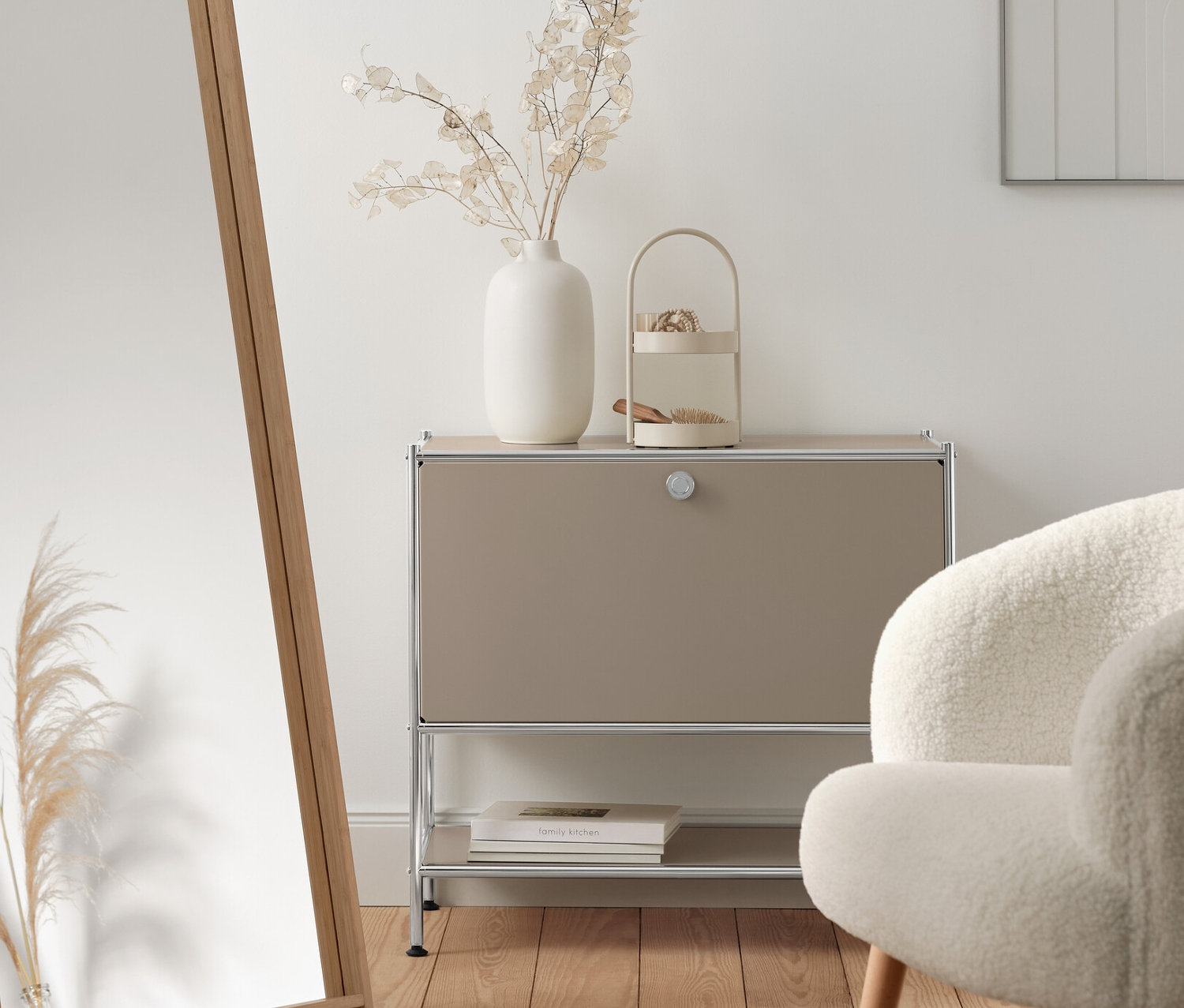 Interiér s béžovým kovovým sideboardem »CN3« s výklopnými dvířky, stojacím zrcadlem s bambusovým rámem a křeslem z buklé s dřevěnými nohami.