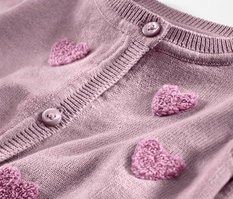 Detail dětského pleteného svetru s našitými růžovými srdíčky a knoflíky.