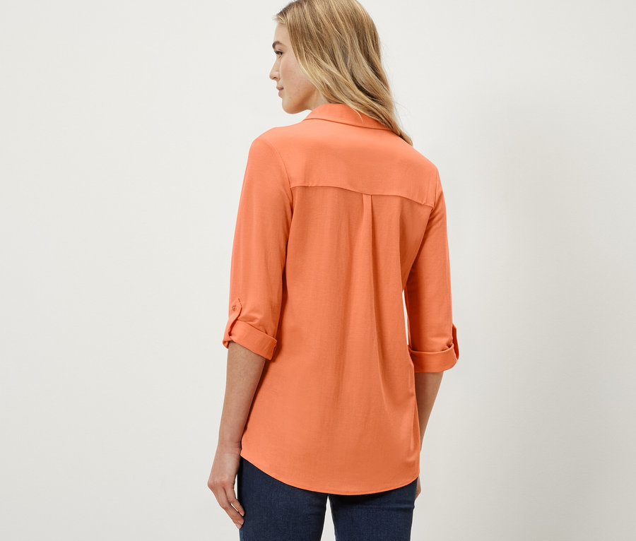 Žena má na sobě broskvovou halenku z žerzejového piké.