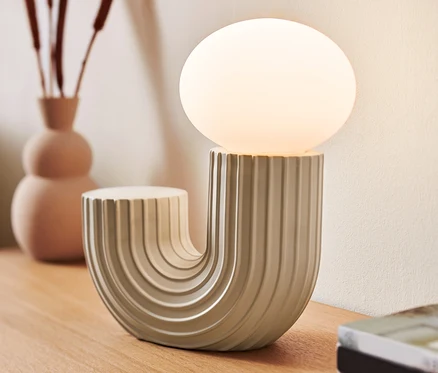 Designová stolní LED lampa stojí na dřevěném stole vedle vázy a knih.