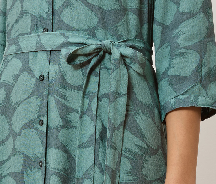 Detail of a turquoise button-down dress with a gray brushstroke pattern and a tied waist.
