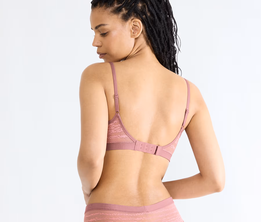 Žena zezadu, má na sobě podprsenku sloggi FREE Evolve PU Lace v barvě date night pink a ladící kalhotky.