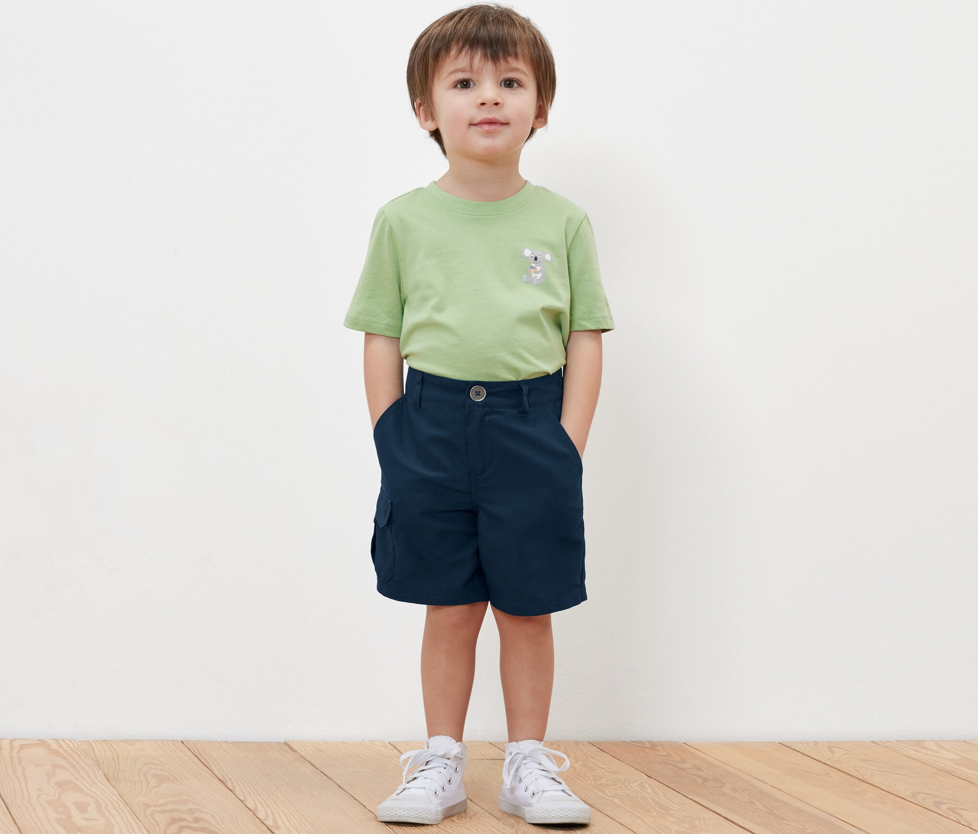 Chlapec stojí a má ruce v kapsách dětských funkčních šortek.