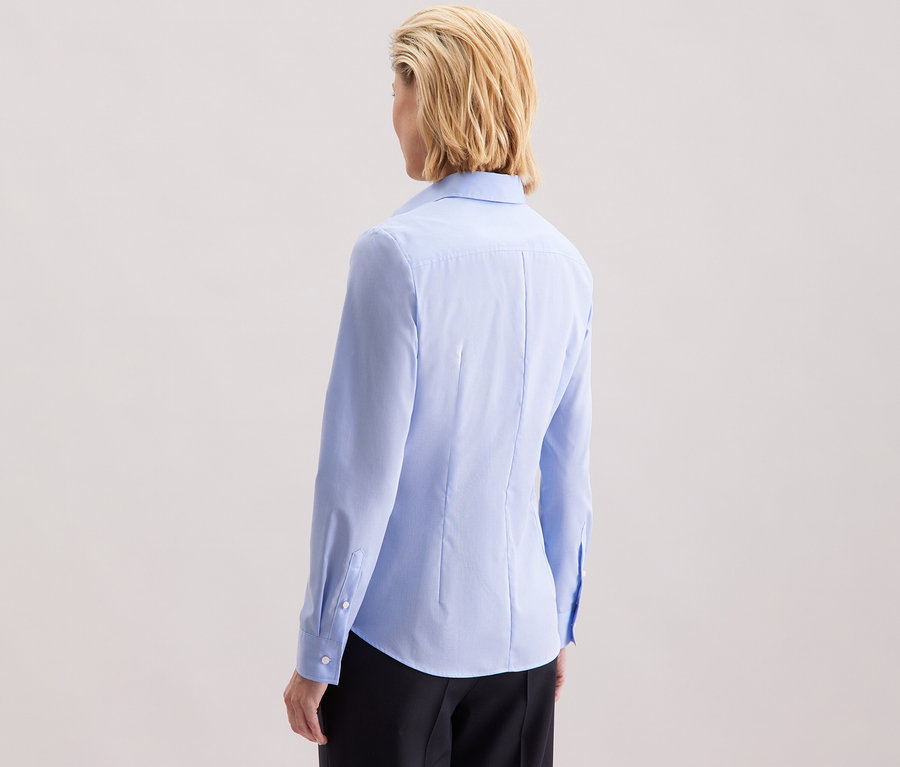 Pohled zezadu na ženu s blond vlasy po ramena v světle modré halence Seidensticker Slim Fit non iron.
