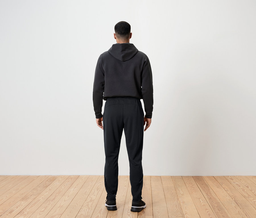 Muž zády ke kameře má na sobě černé kalhoty a mikinu s kapucí.
