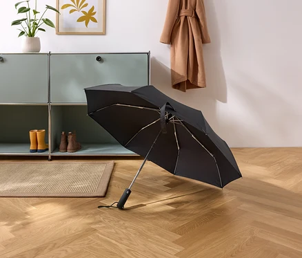 Černý deštník leží na parketové podlaze v chodbě.