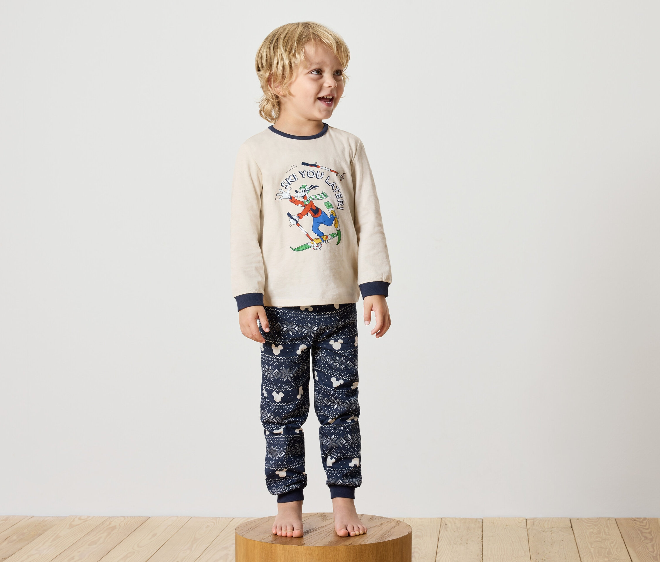Chlapec stojí na dřevěném podstavci a má na sobě pyžamo s motivem Disney.
