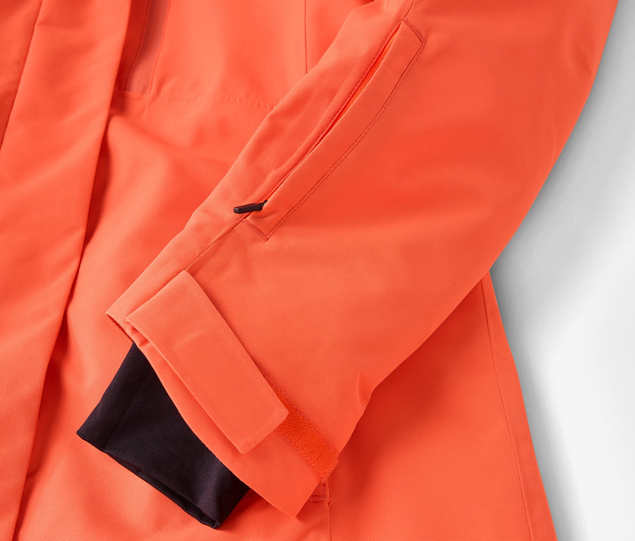 Detail oranžové bundy s černou manžetou a kapsou na zip.