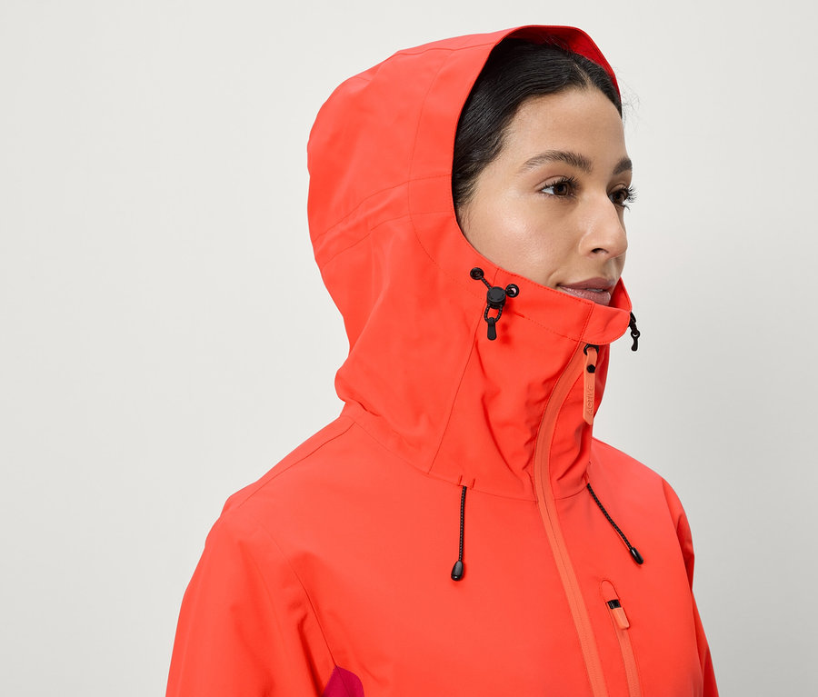 Žena má na sobě korálově červenou bundu s kapucí.