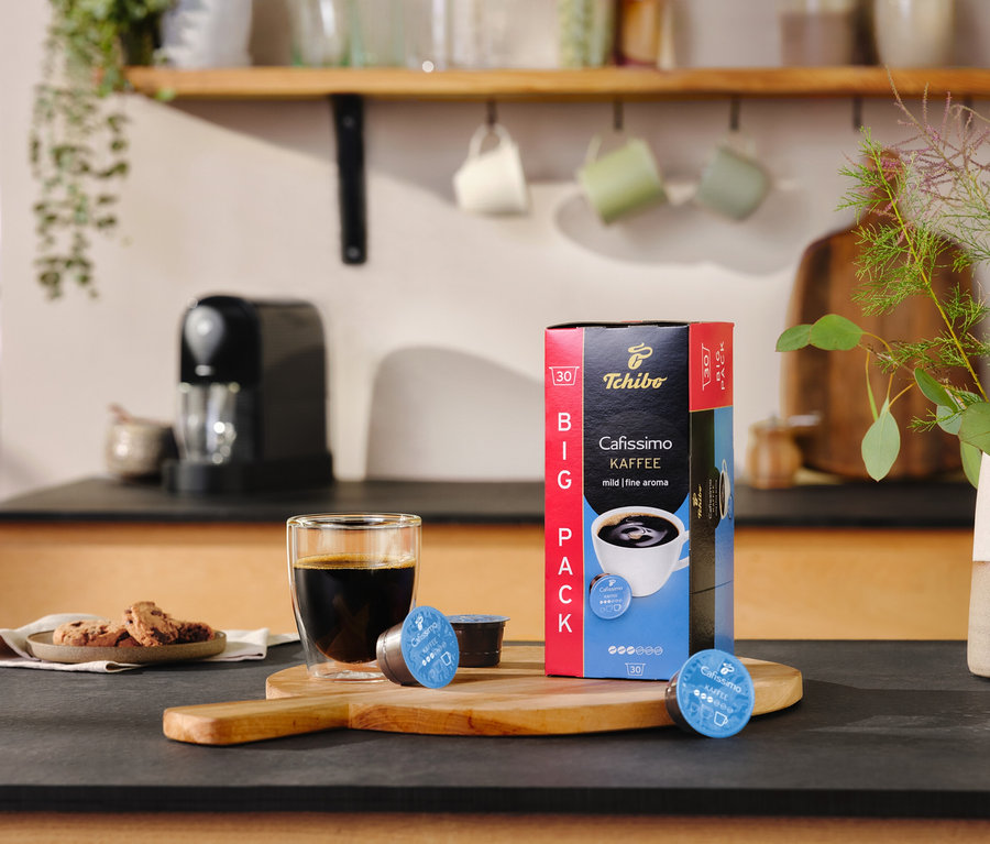 Na lince stojí sklenice s kávou vedle balíčku Cafissimo pure+, black a dvou kapslí.