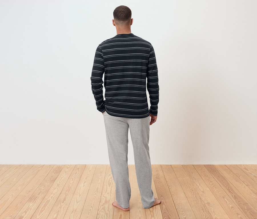 Muž zády k fotoaparátu má na sobě pruhované tričko s dlouhým rukávem a šedé tepláky.