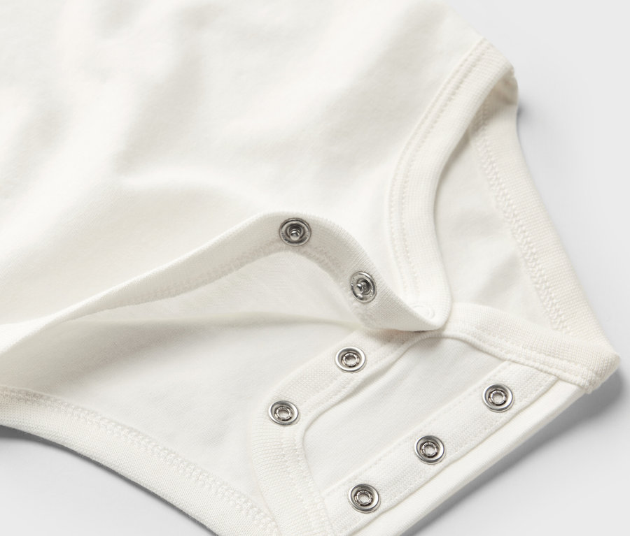 Detail bílého rostoucího body pro miminka s patentkami.