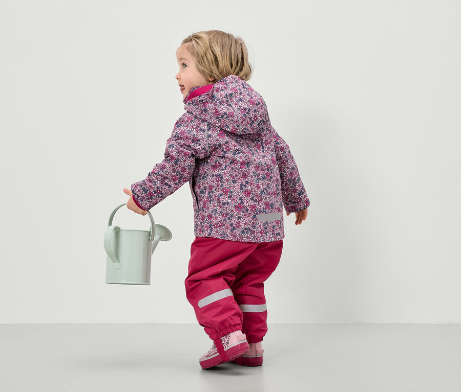 Dítě v květinové bundě a růžových kalhotách drží konev.
