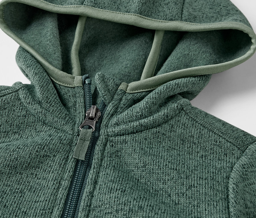 Detail dětské mikiny z pleteného fleecu se zipem a kapucí.