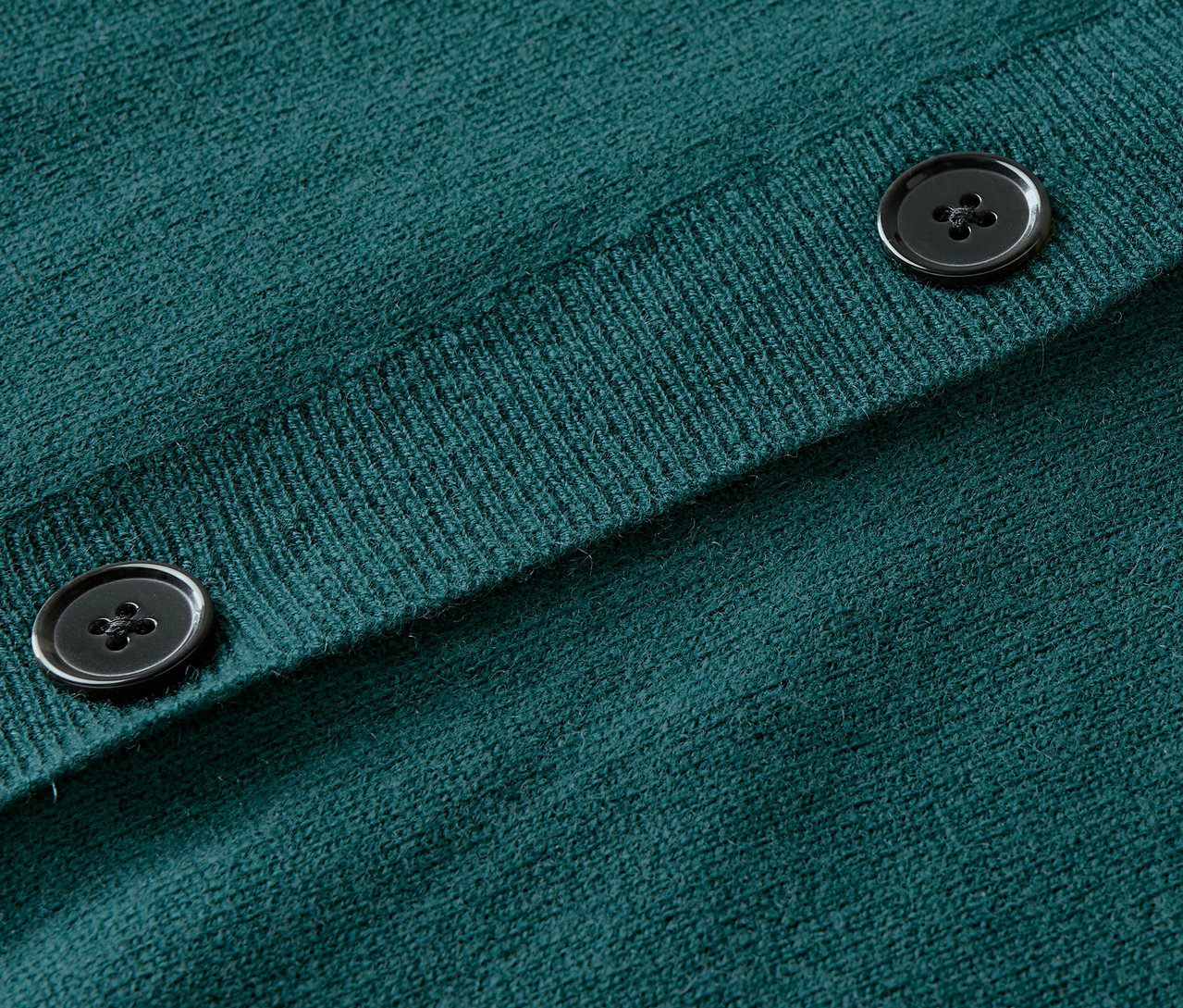 Detailní záběr na zelený pletený svetr s knoflíky.